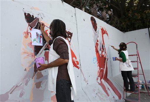 Aug. 20, 2015 photo, independent Afghan artist Kabir Mokamel, left, paints on a barrier wall which blocks a main gate of the presidential palace in Kabul, Afghanistan